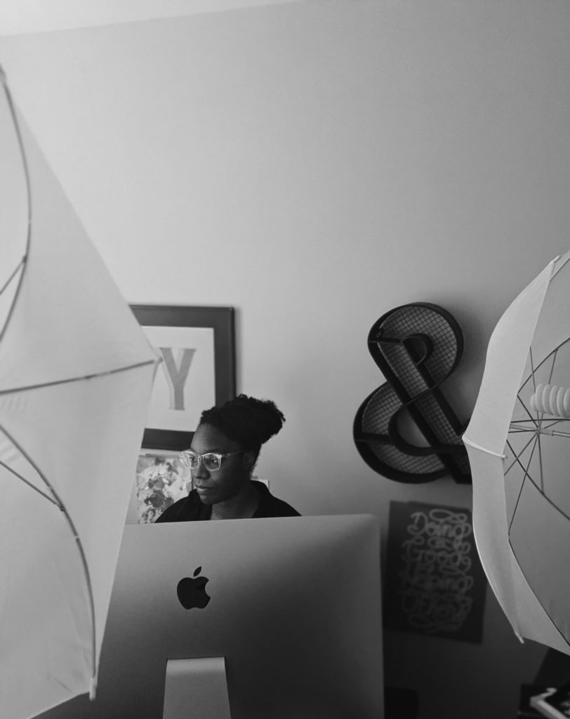 Woman in an office with an ampersand behind her and surrounded by lights