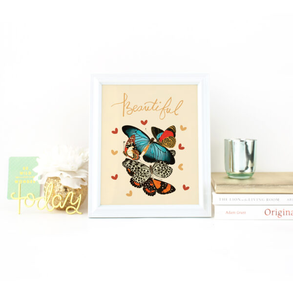 The word beautiful handlettered above a vintage botanical illustration of butterflies surrounded by hearts on a white desk