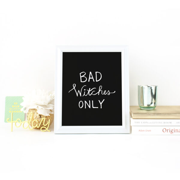 Bad Witches Only handlettered in white on a black background in a white frame on a desk