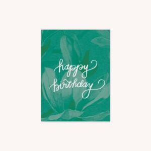 A birthday card with a green magnolia background with Happy Birthday handlettered in white