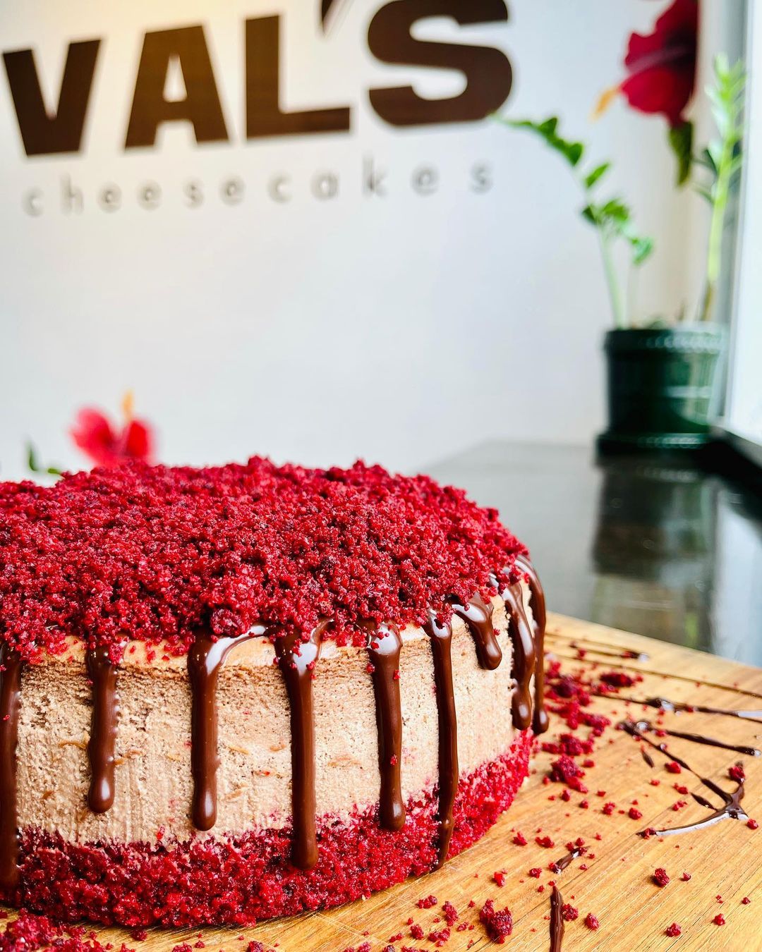 Photo of red velvet cheesecake in front of bakery sign that says Val's