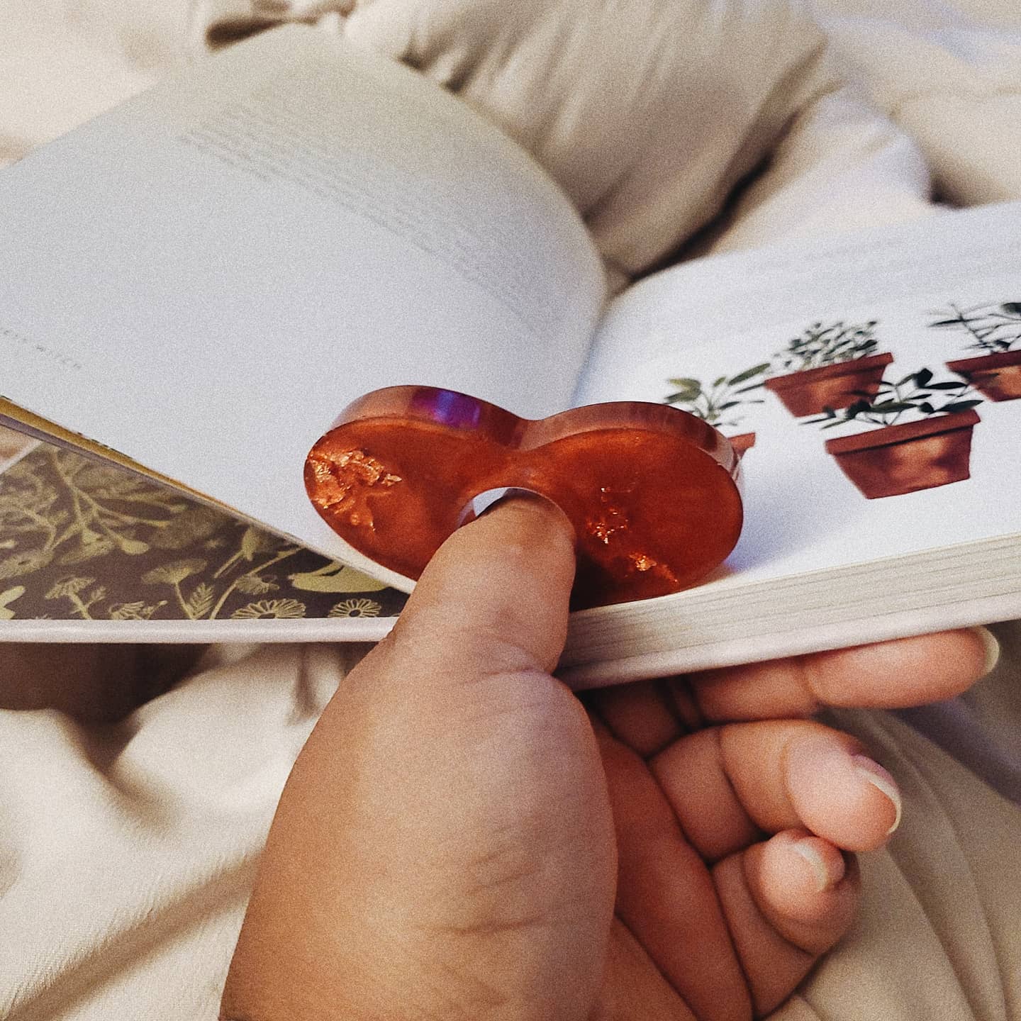 Image of hand holding a red heart bookholder to keep their book open while reading in bed