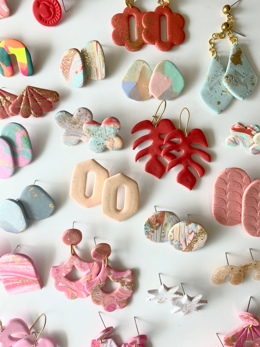 Several different pairs of different styled earrings in hues of reds, pinks, and blues